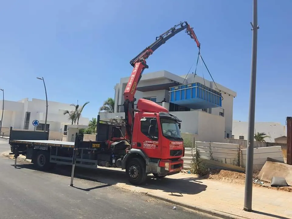 משאית מנוף מניפה מטען גדול לצד מבנה